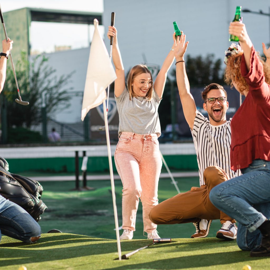 Group of smiling friends enjoying together playing mini golf in the city.